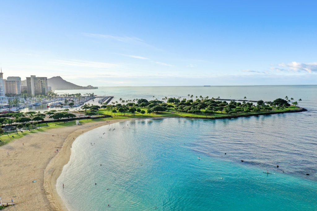 Aerial shot of Honolulu with Diamond Head, marina, and sandy beach under a clear blue sky.