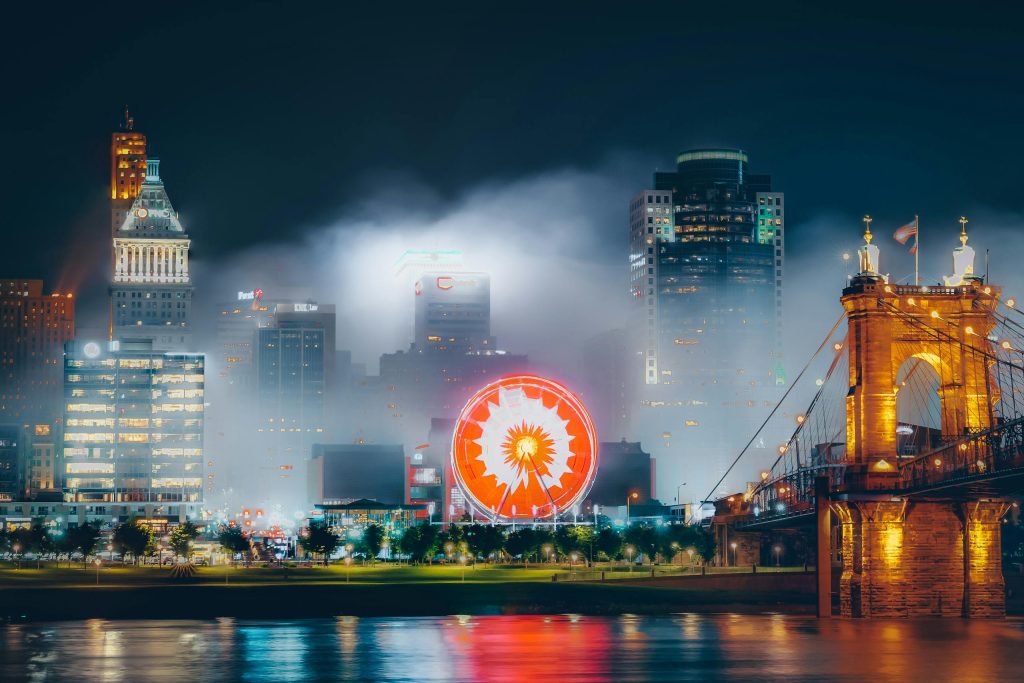 Dramatic view of Cincinnati's skyline at night with illuminated buildings and ferris wheel reflections.