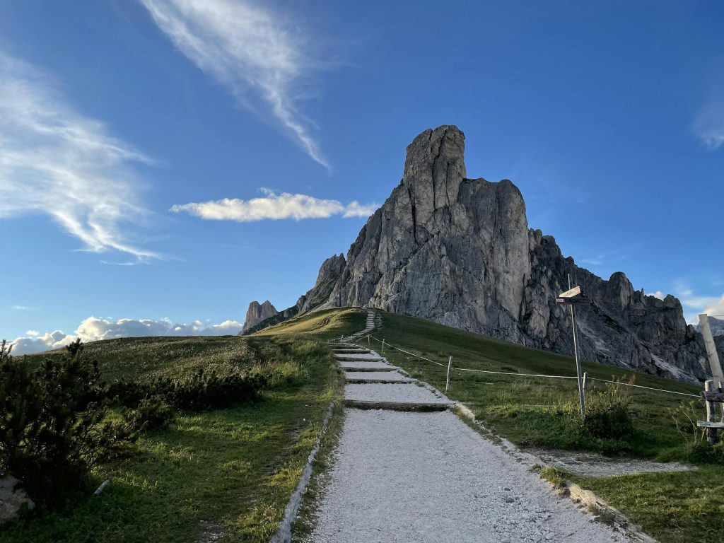 Path leading to the majestic rocky peaks of Giau Pass under a clear blue sky, Italy.