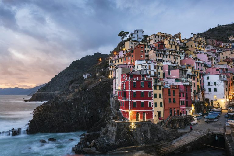Scenic view of Riomaggiore's vibrant houses on a cliffside at sunset, Liguria, Italy.