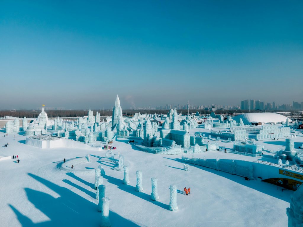 Stunning aerial view of Harbin Ice and Snow Festival with intricate ice sculptures under a clear blue sky.