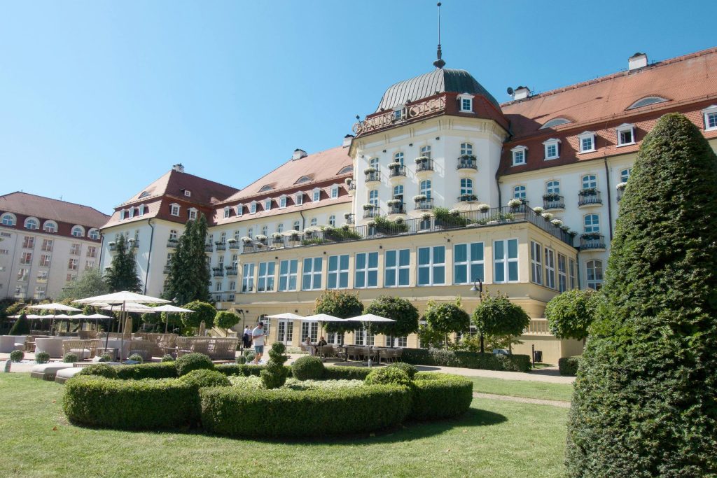Stunning historic hotel exterior with lush gardens and classic architecture under a bright blue sky.