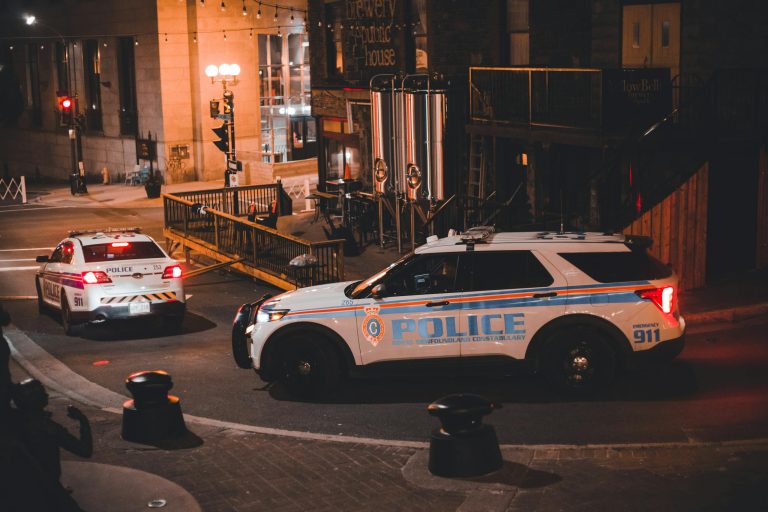 Two police cars patrolling a city street at night with warm lighting creating a dramatic urban mood.