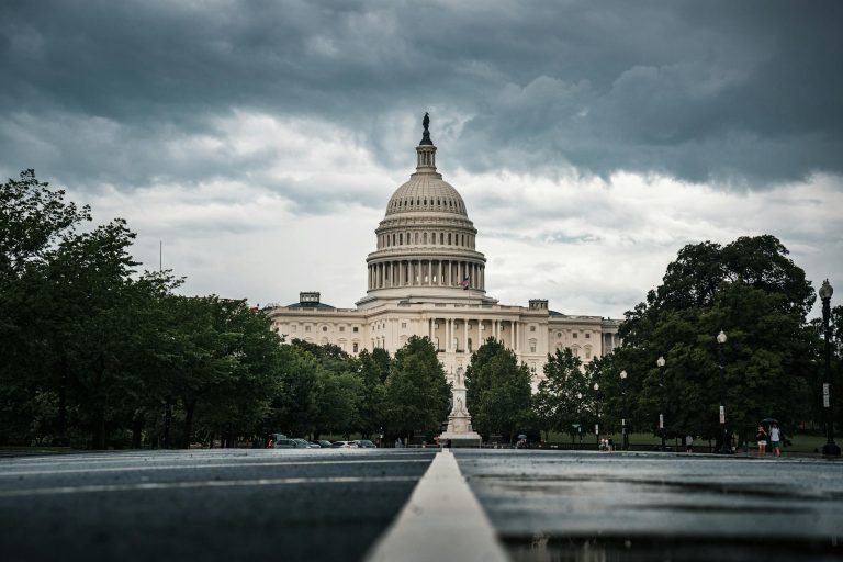US Capitol Building surrounded by lush trees under dramatic cloudy skies in Washington, DC.