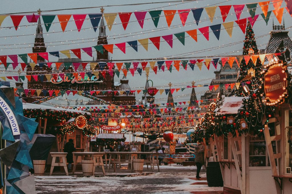 Vibrant and festive Christmas market with flags, lights, and decorations in a snowy setting.