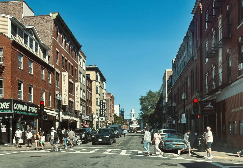 Vibrant street view of Hanover Street in Boston's North End with pedestrians and red brick buildings.