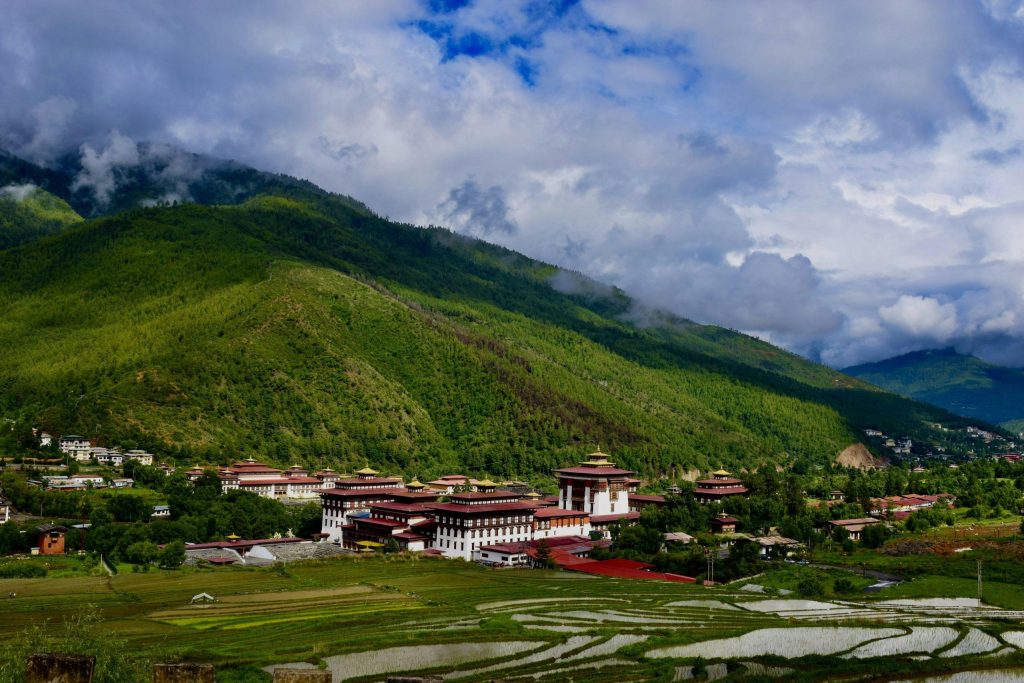 A breathtaking view of the Tashichho Dzong in Thimphu valley, surrounded by lush green mountains under a cloudy sky.