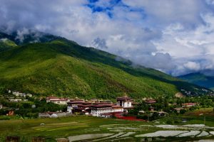 A breathtaking view of the Tashichho Dzong in Thimphu valley, surrounded by lush green mountains under a cloudy sky.