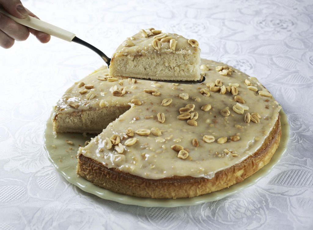 A close-up of a peanut butter cake being sliced on a white tablecloth, perfect for dessert lovers.