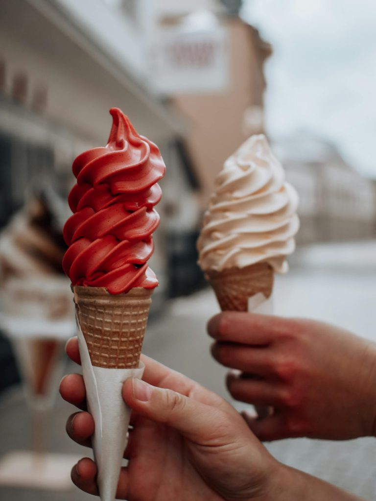 A detailed view of hands holding colorful ice cream cones in an outdoor setting.