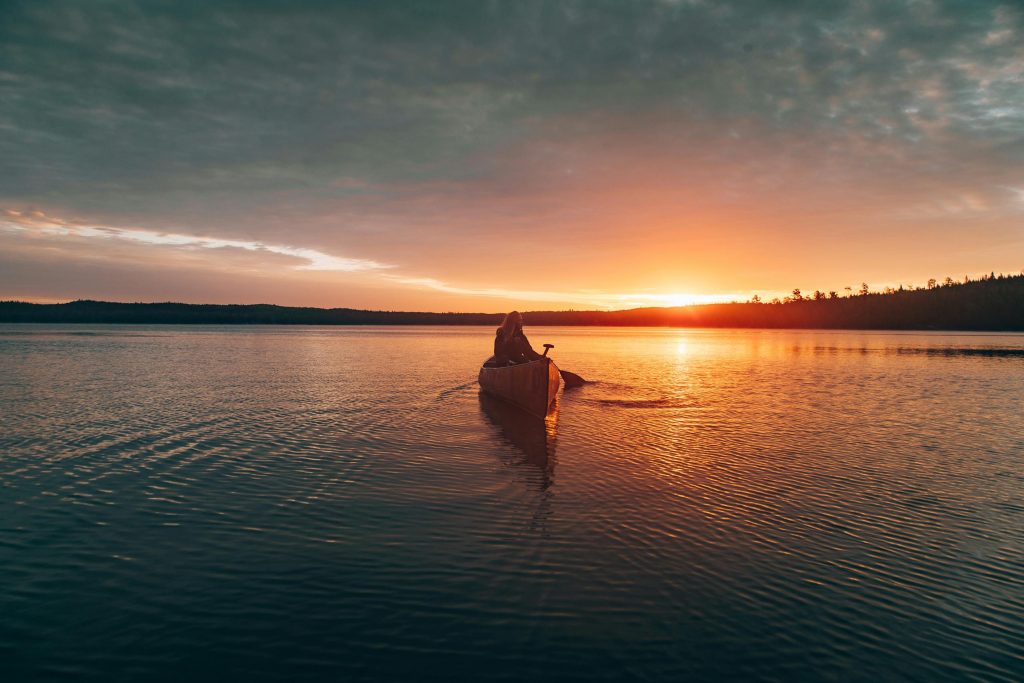 A lone canoeist paddling on Ely Lake at sunset, capturing nature's serene beauty.