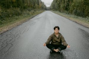 A man practices meditation in a yoga pose on a quiet forest road, emphasizing mindfulness and well-being.