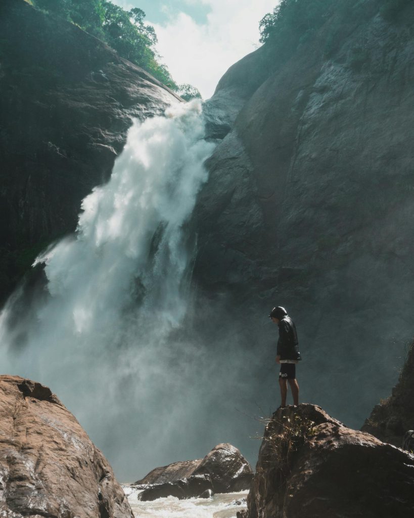 A man standing near a breathtaking waterfall in Badulla, Sri Lanka, showcasing nature's beauty and adventure.