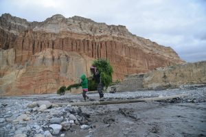 A mother and child walk across a rocky landscape in Upper Mustang, Nepal with a steep cliff backdrop.