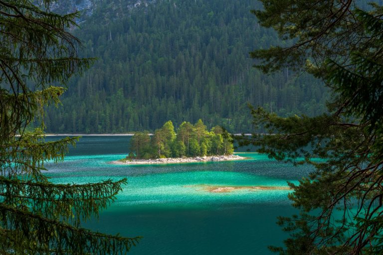 A peaceful islet surrounded by turquoise waters in an alpine lake, framed by evergreen trees.