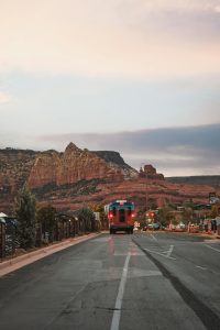 A picturesque view of a bus traveling through Sedona's stunning red rock landscape at sunset.