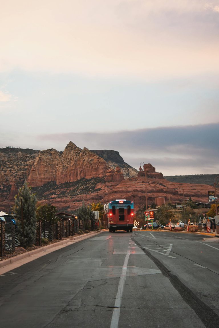 A picturesque view of a bus traveling through Sedona's stunning red rock landscape at sunset.