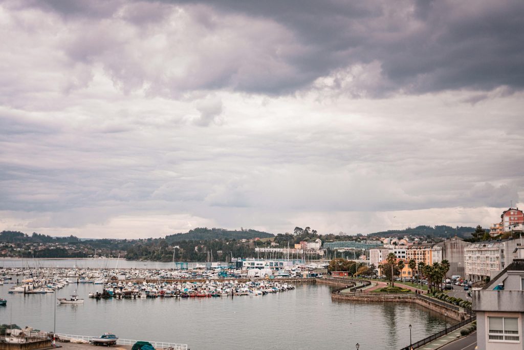 A picturesque view of Sada harbor in Galicia, Spain with moored boats under a cloudy sky.