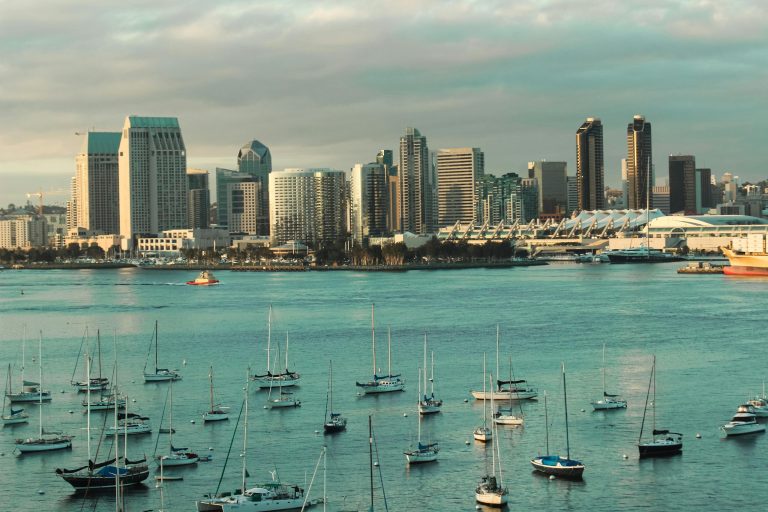 A picturesque view of the San Diego skyline with sailboats anchored in the harbor under a cloudy sky.