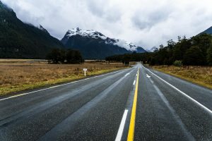 A scenic mountain road in New Zealand with snow-capped peaks and lush greenery.