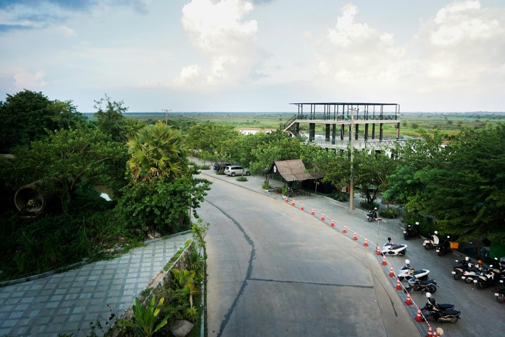 A serene roadside view featuring lush greenery and a modern building near Phnom Penh, Cambodia.