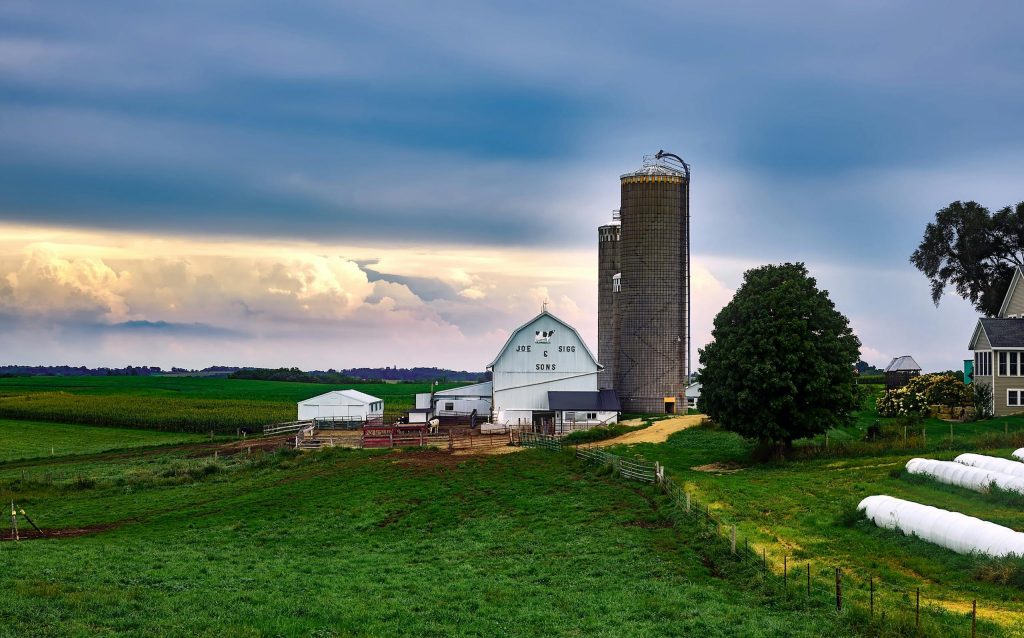 A serene view of a traditional farm with a barn and silo under dramatic sunset skies in Wisconsin countryside.