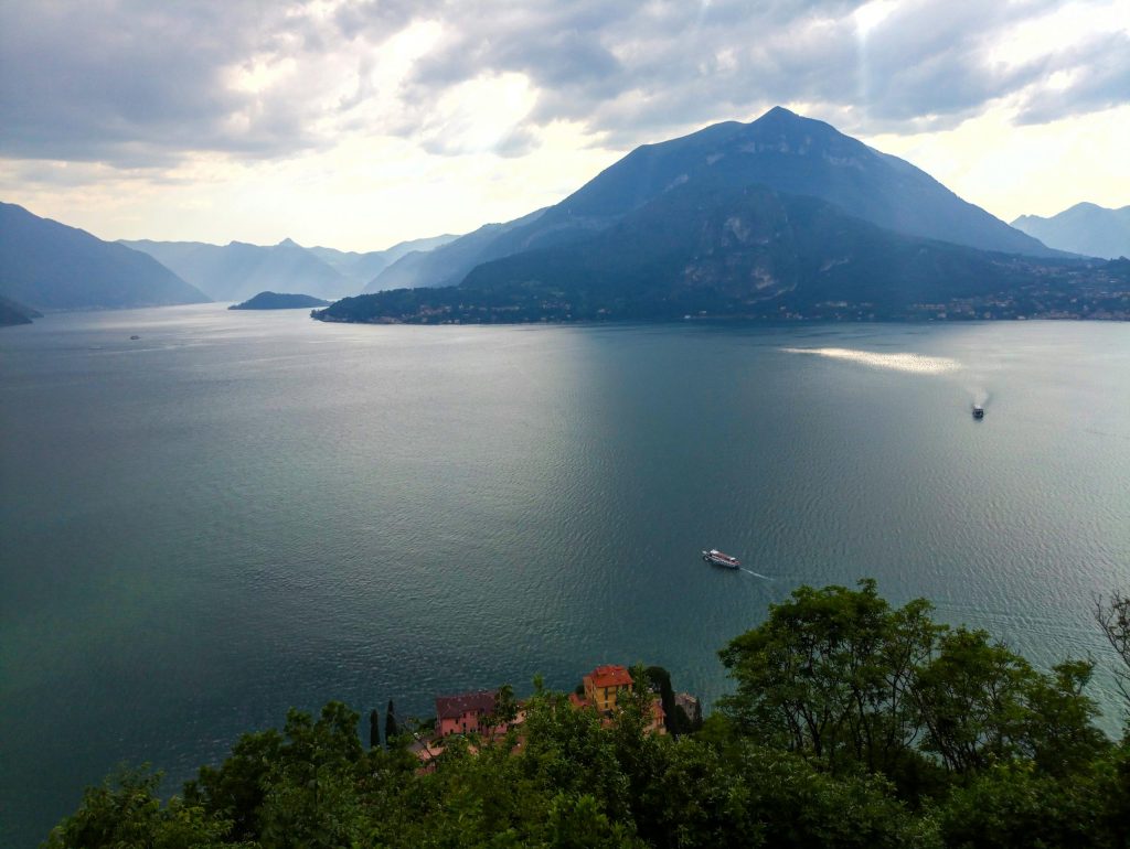 A serene view of Lake Como in Italy with mountains and boats under cloudy skies.