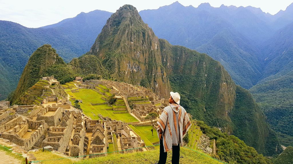 A tourist in traditional attire gazes at the breathtaking view of Machu Picchu ruins in Peru.