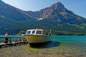 A tranquil scene with a moored boat at a lakeside, surrounded by majestic mountains and clear blue water.