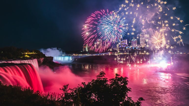 A vibrant fireworks display illuminates the night sky over Niagara Falls, showcasing the stunning waterfalls and city lights.