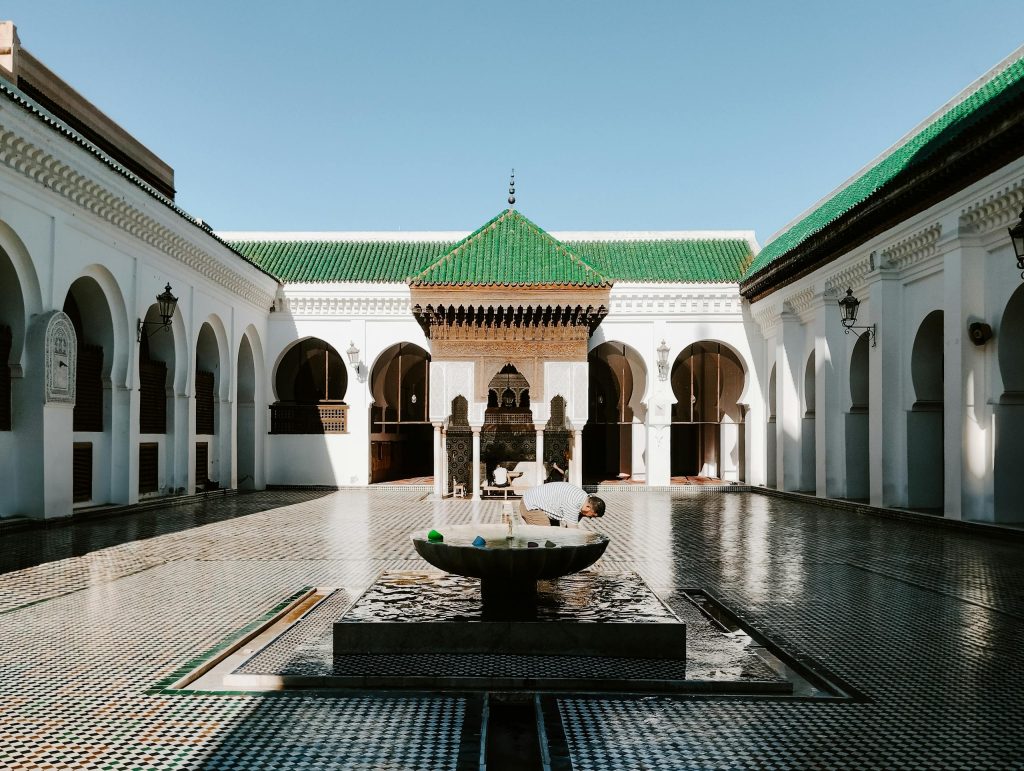 A view of the historic Al Quaraouiyine Mosque courtyard in Fes, Morocco with traditional architecture and ornate fountain.
