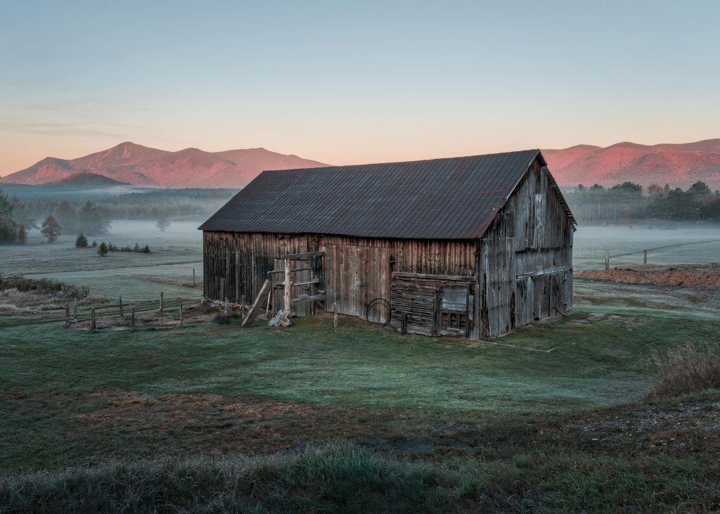 A vintage barn set against the misty Adirondack mountains at sunrise in Wilmington, New York.