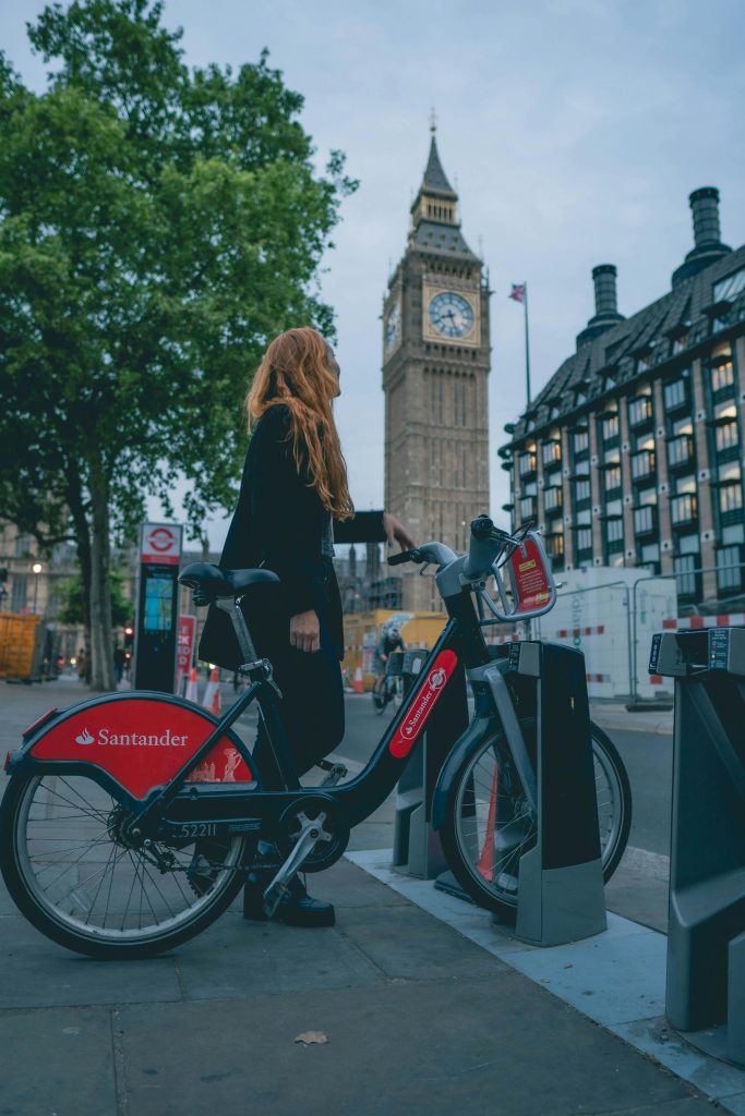 A woman renting a Santander bike near Big Ben, London, showcasing urban mobility and iconic landmarks.