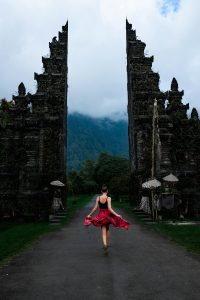 A woman twirls in a red dress at the famous Handara Gate in Bali, Indonesia, amidst misty mountains.