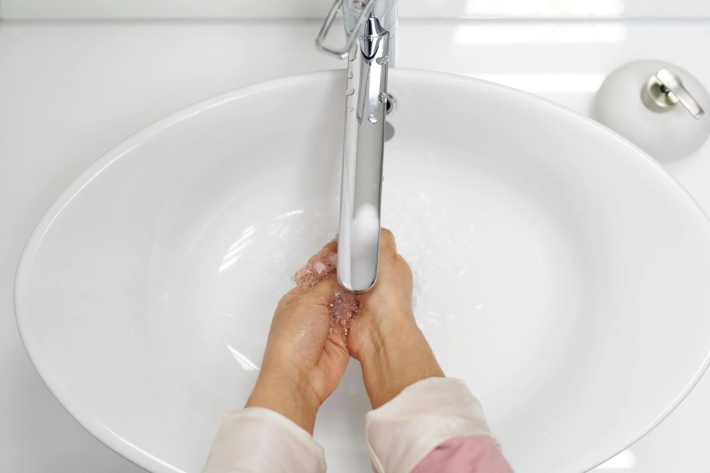 A woman washing her hands under a chrome faucet in a white sink, emphasizing hygiene.