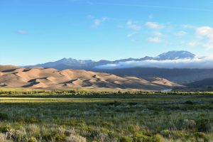 Beautiful landscape of Great Sand Dunes with mountain backdrop under a clear sky.