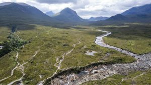 Breathtaking aerial view of the Scottish Highlands with rolling hills and a winding river under a cloudy sky.