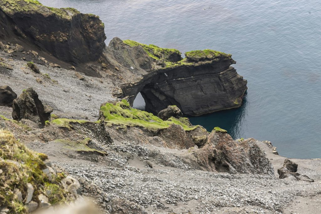 Breathtaking view of Iceland's rocky coastal cliffs with vibrant green moss and clear ocean waters.