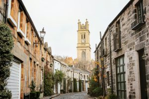 Charming cobblestone street in Edinburgh showcasing St Stephen's Church tower amidst historic architecture.
