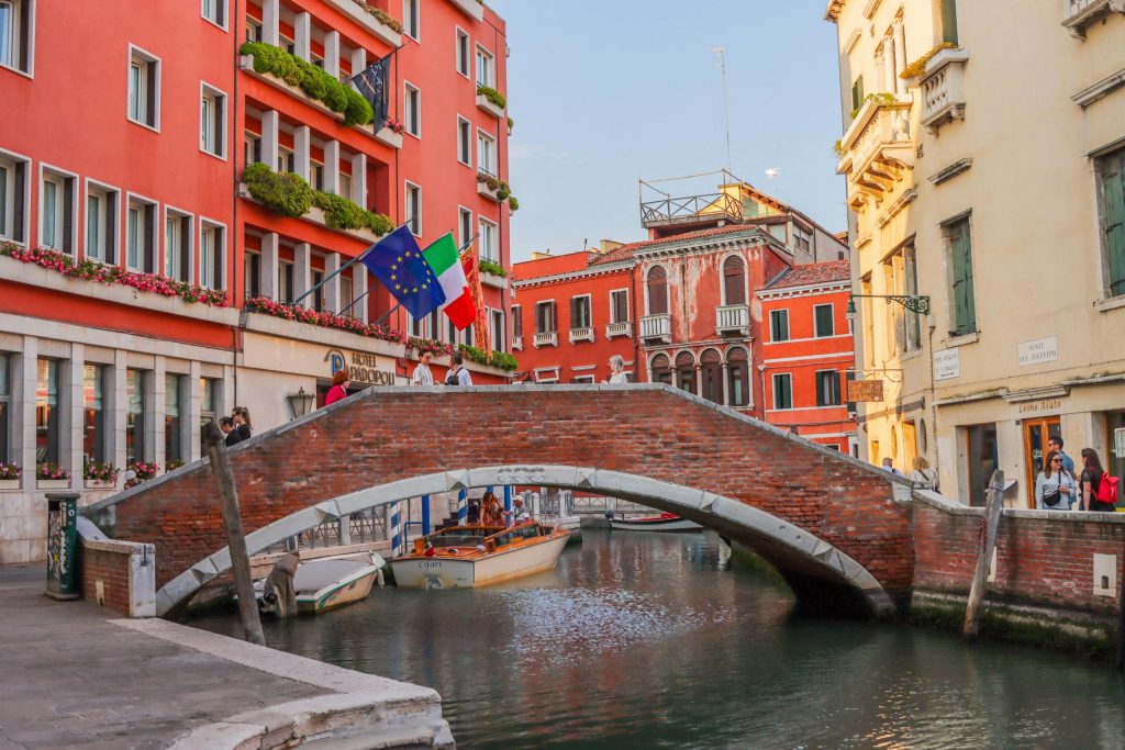 Charming view of a Venetian canal with traditional architecture, bridge, and flags in Venice, Italy.
