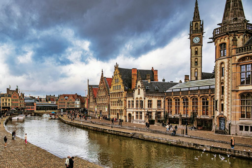 Charming view of Ghent's historic architecture along the water under dramatic skies.