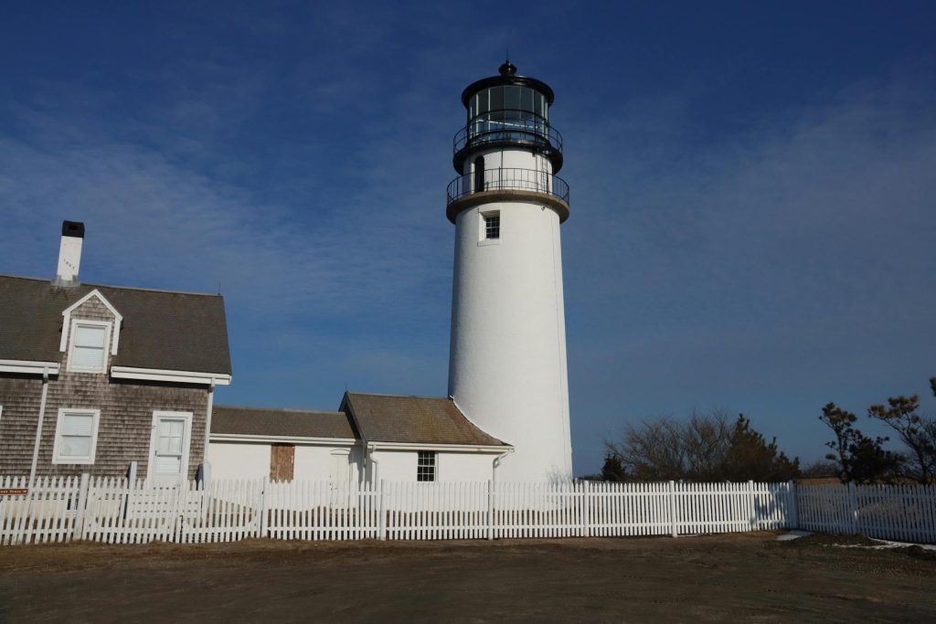 Classic Cape Cod lighthouse at sunrise in Truro, MA, with white picket fence and clear sky.