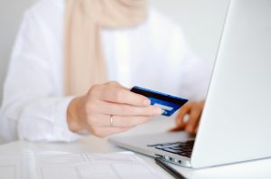 Close-up of a person holding a credit card while using a laptop for online shopping.