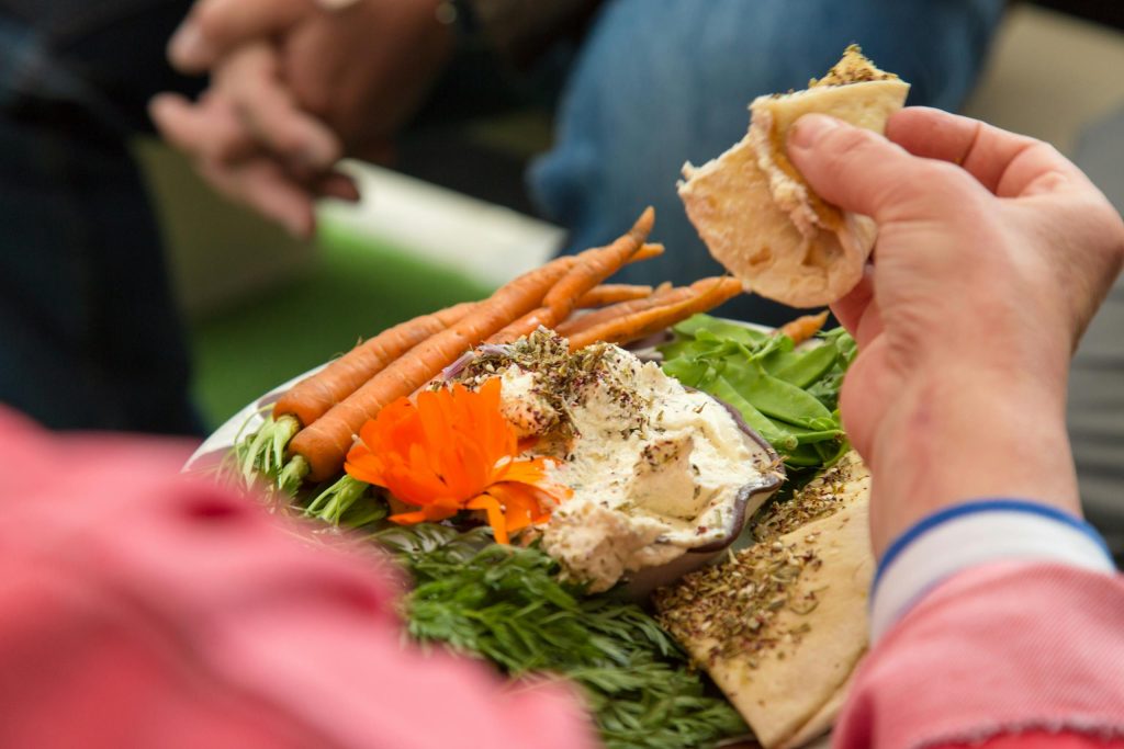 Close-up of hands enjoying hummus with fresh vegetables and pita bread, showcasing healthy eating.