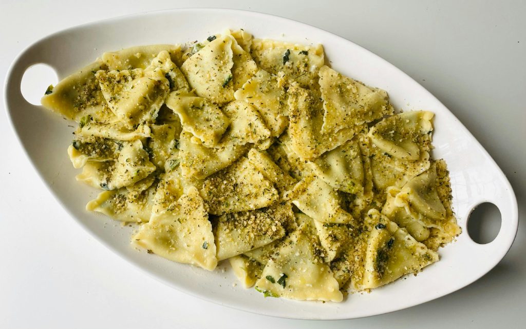 Close-up of homemade pesto pasta on a white ceramic plate, garnished with herbs.