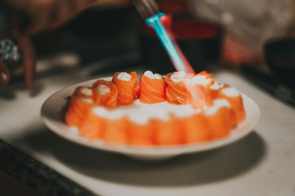Close-up of torched salmon sushi pieces arranged on a ceramic plate with blurred background.