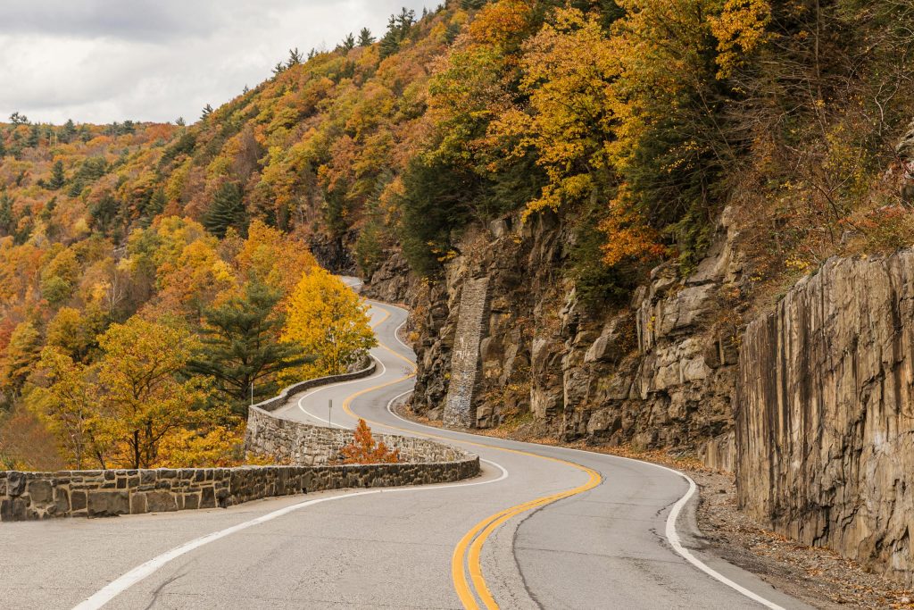 Curvy mountain road with vibrant fall foliage in New York's forested landscape.