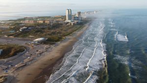 Drone shot of South Padre Island beach with waves and buildings along the coast.