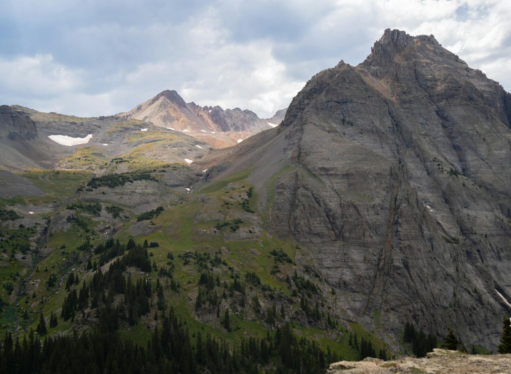 Explore the breathtaking mountain peaks of Colorado's San Juan Range with lush green valleys and rugged rock formations.