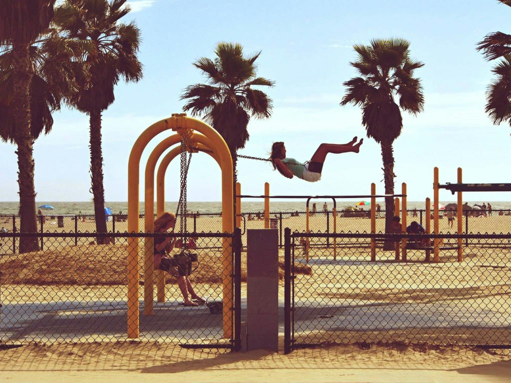 Kids enjoying a swing set by palm trees at Venice Beach, Los Angeles, California.